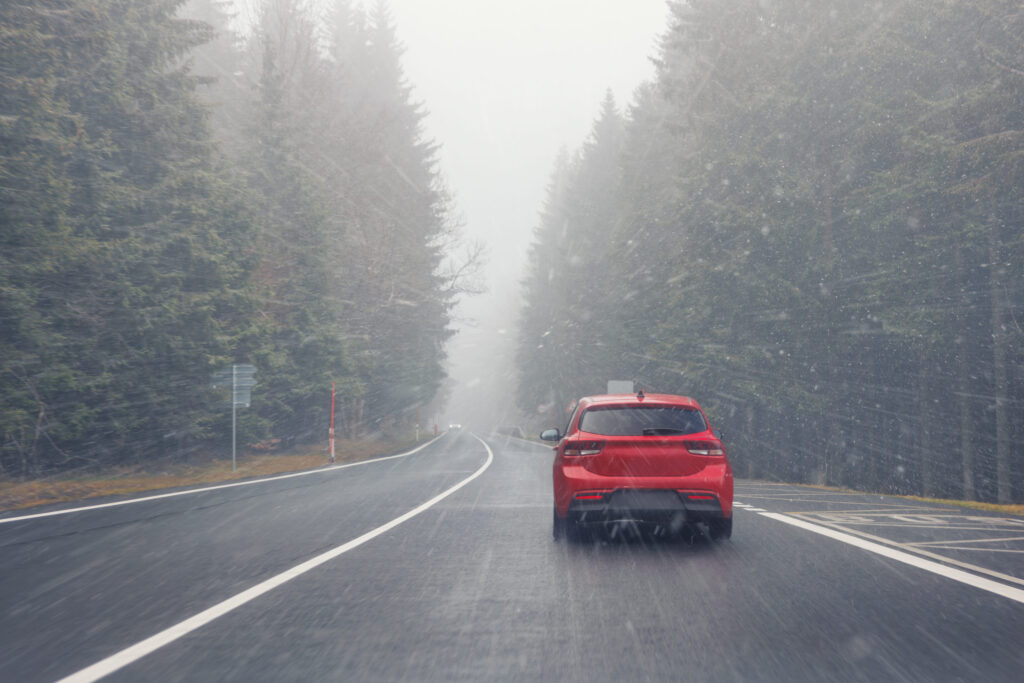Automobil jazdiaci po mokrej zimnej ceste bez súvislej snehovej pokrývky.